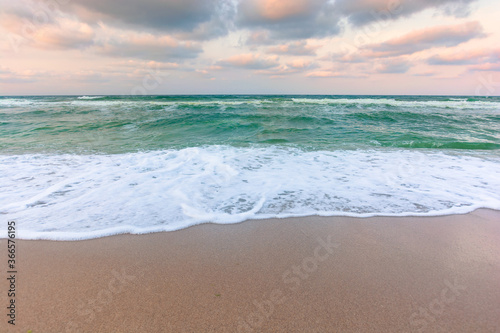 cloudy sunset sea side. waves running the sandy beach. changing windy weather in evening light photo