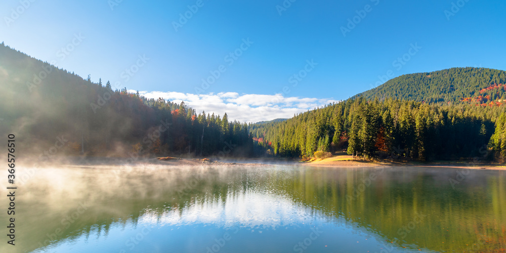 lake landscape at foggy sunrise. misty scenery reflecting in the water. wonderful autumn morning in fall season. trees in colorful foliage