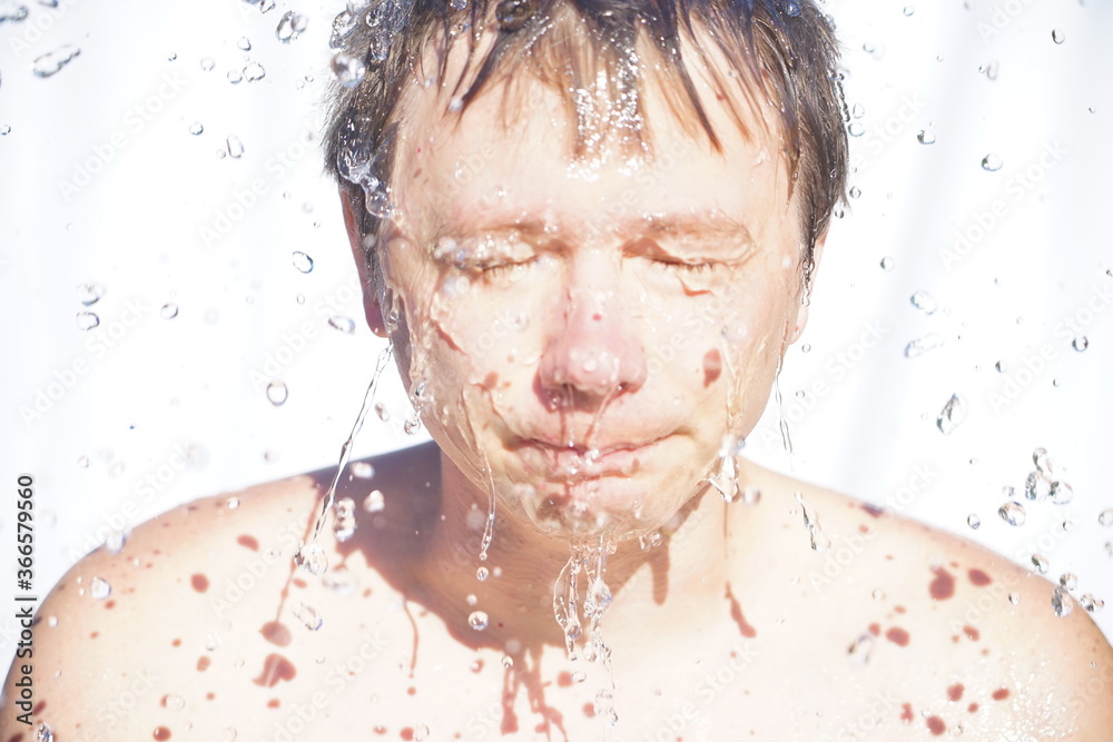 The guy washes his face with water, drops fly in different directions, on a white background