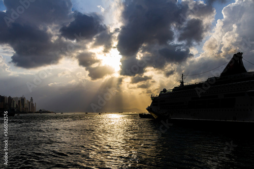 Silhouette of a cruise ship in the evening with cloudy weather and the light rays coming out through the clouds and reflect water.