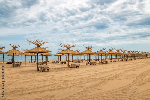Beauty wooden umbrellas and sunbeds in a row of empty sandy beach