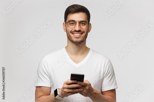 Handsome man isolated on gray background, looking straight at camera while holding his phone © Damir Khabirov