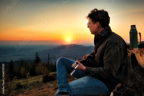 Ein Junge spielt Gitarre und schaut dem Sonnenuntergang entgegen