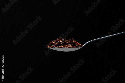 Isolated spoon full of chilli pepper in a black background