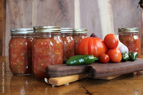fresh tomatoes and jalapenos from a family farm vegetable garden with garlic and red onion for home canned spicy salsa in glass jars on a rustic background