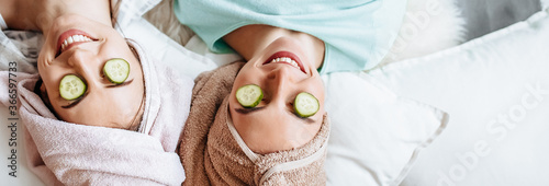 Two girls make homemade face and hair beauty masks. Cucumbers for the freshness of the skin around the eyes. Women take care of youthful skin. Girlfriends laugh at home lying on the floor on pillows.