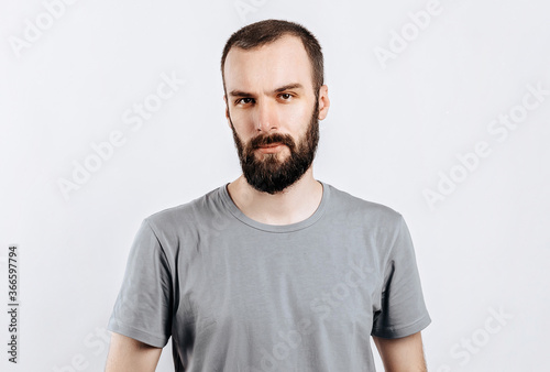 A handsome brutal brunette man with a beard in a gray shirt looks seriously at the camera. Place for advertising on a gray background.