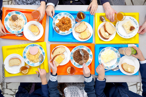 Children are having lunch in the school cafeteria. Top view of dishes on colored trays.