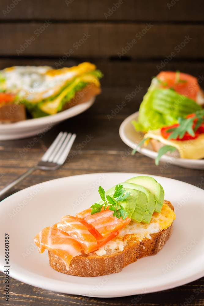 Different delicious sandwiches for breakfast, bread with cheese, avocado and trout, sandwich with egg, tomato and rucola, parsley