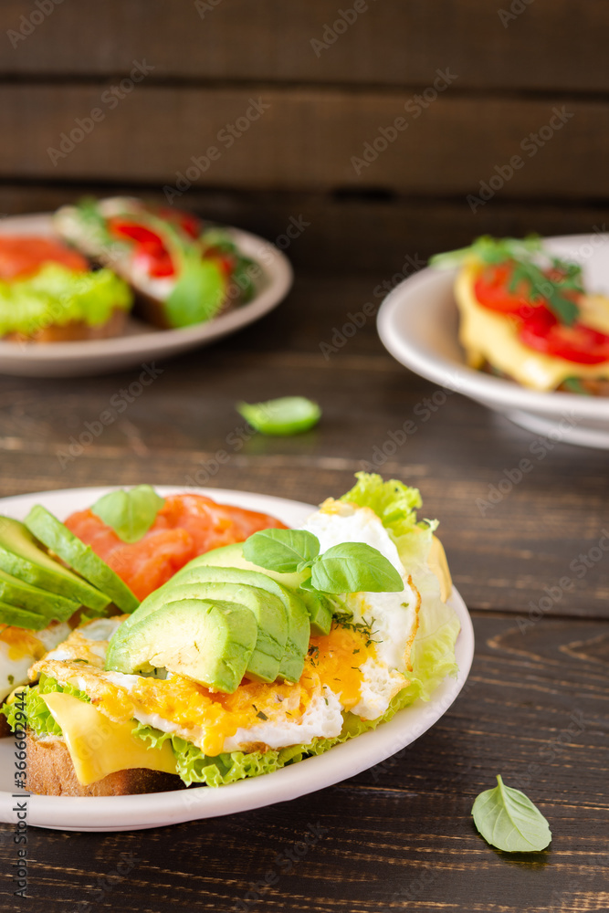 Different delicious sandwiches for breakfast, bread with cheese, avocado and trout, sandwich with egg, tomato and rucola, parsley with basil Different delicious sandwiches for breakfast, bread with cheese, avocado and trout, sandwich with egg, tomato and rucola, parsley with basil