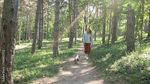 Attractive blonde haired woman walking with her dog, cavalier king charles spaniel, in the park. Having fun together.
