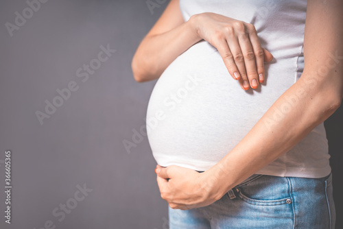 Pregnant woman holds hands on belly on a gray background. Copy space, pregnancy, motherhood, people and expectation concept. Close-up, copy space, indoors. Toned photo of pregnancy.