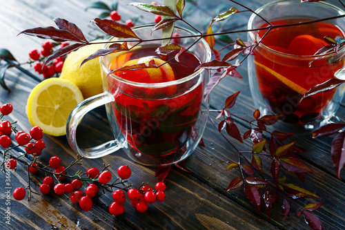 Two transparent glass cups of hot berry tea with lemons  in autumn leaves decoration, winter autumn mood, citrus red tea, autumn concept, rain drops