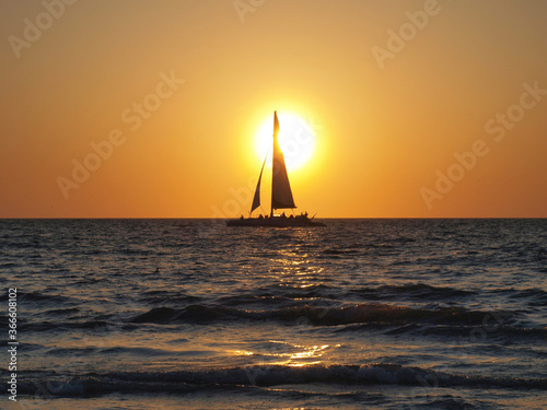 Sunset Sailing on the ocean with bright orange-red sky with large sun receding behind to portray a silhouette of a sailboat