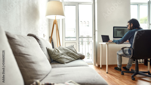 Home office. Rear view of young man, software developer writing code on laptop while sitting at his workplace and working from home photo