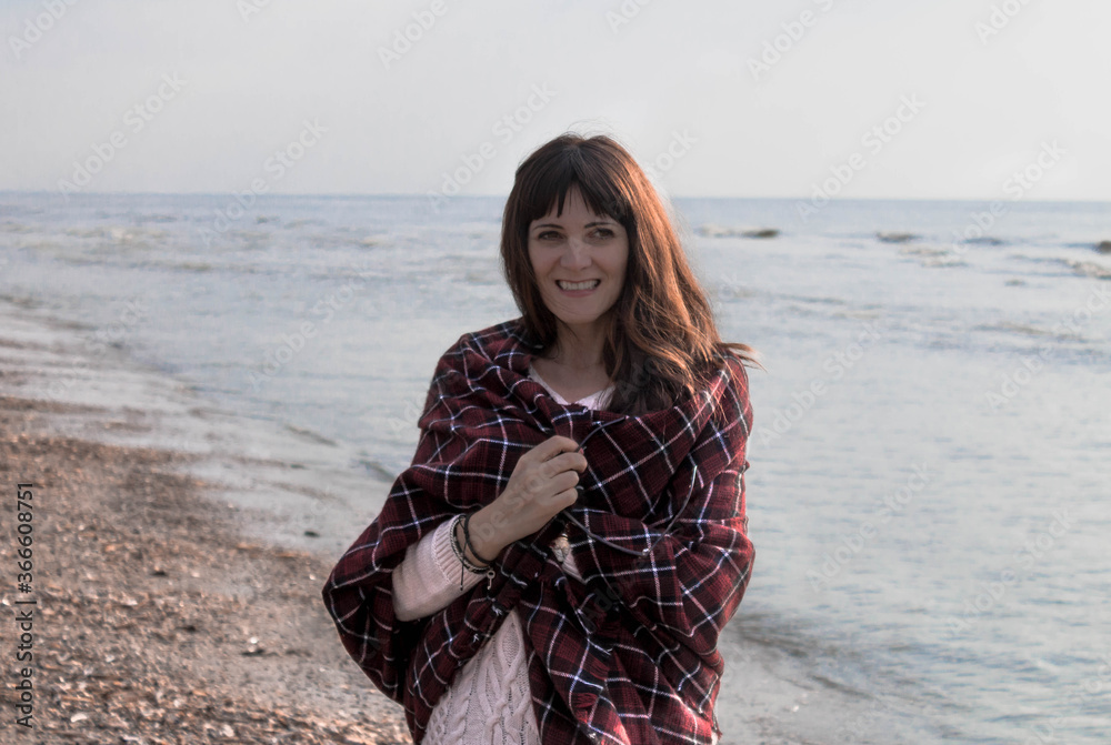 Beautiful happy girl walking along the ocean / sea shore at sunset, wrapped in a trendy checkered scarf.Girl on the beach. Beautiful happy girl walking along the ocean / sea shore at sunset, wrapped in a trendy checkered scarf.Girl on the beach.