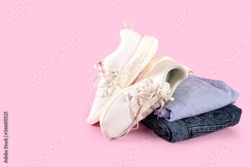 Woman's casual summer clothes with white textile sneakers on pink background, sport running shoes with white soles, with copy space
