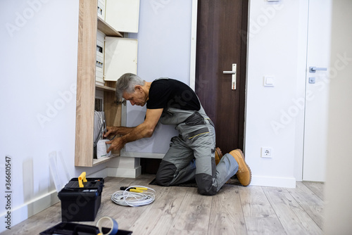 Full length shot of aged electrician, repairman in uniform working, installing an ethernet cable for router in fuse box