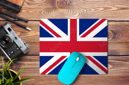 United Kingdom flag on wooden background with blue wireless mouse on a mouse pad, top view. Digital media concept. photo