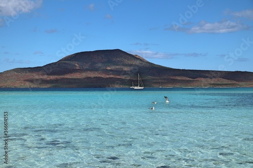 Baja Californian turquoise bay with sail boat and green-brown hill in the back