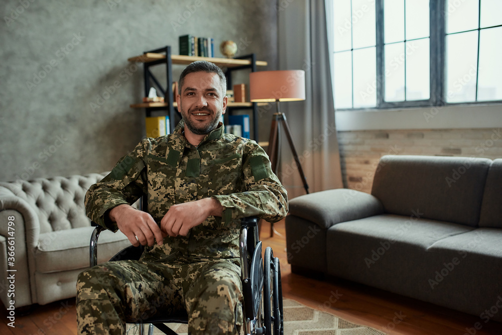 Recovery. Middle aged male military in a wheelchair looking at camera with a smile, during therapy session. Disabled soldier suffering from depression, psychological trauma. PTSD concept