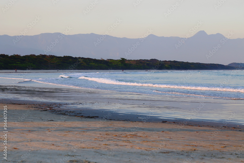 Blue ocean with calm waves. In the background vegetation and far away mountains. Itaguare beach, Bertioga, Brazil Blue ocean with calm waves. In the background vegetation and far away mountains. Itaguare beach, Bertioga, Brazil