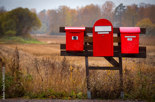 Three red mailboxes in the countryside near an autumn field