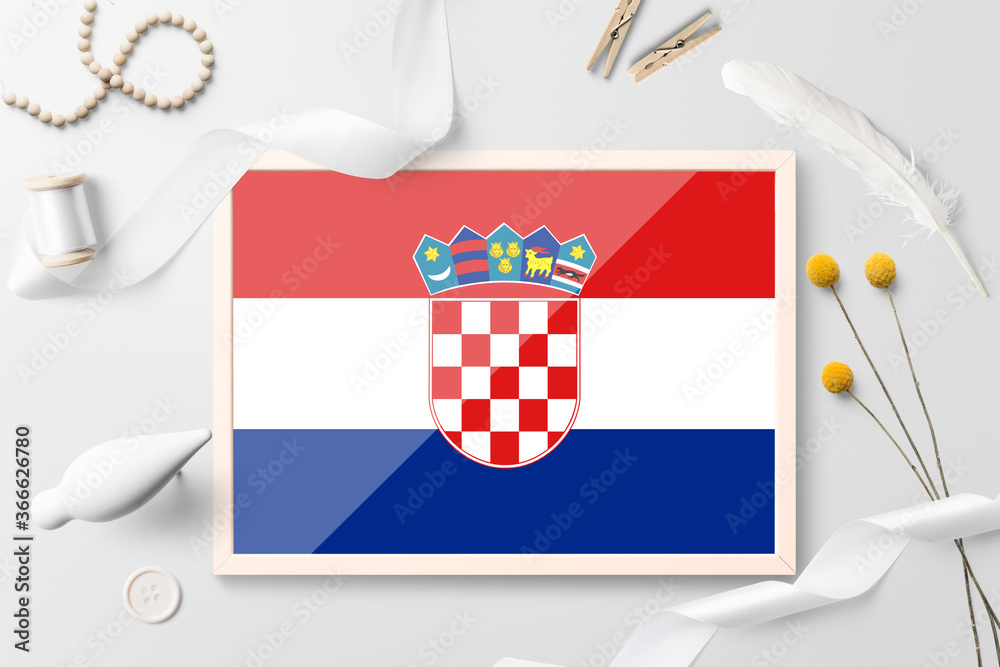 Naklejka premium Croatia flag in wooden frame on white creative background. White theme, feather, daisy, button, ribbon objects.