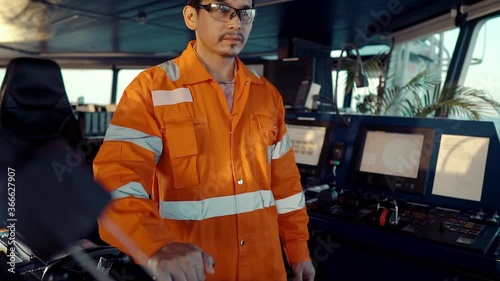 Filipino deck Officer on bridge of vessel or ship wearing coverall during navigaton watch at sea . He is maneuvering with cpp thrusters propulsion photo