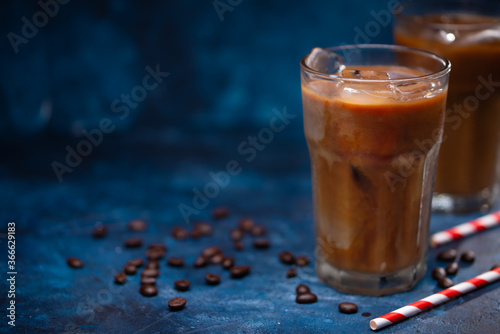 Cold summer drink, iced coffee with cream or milk.Cool drink with coffee grains on blue background