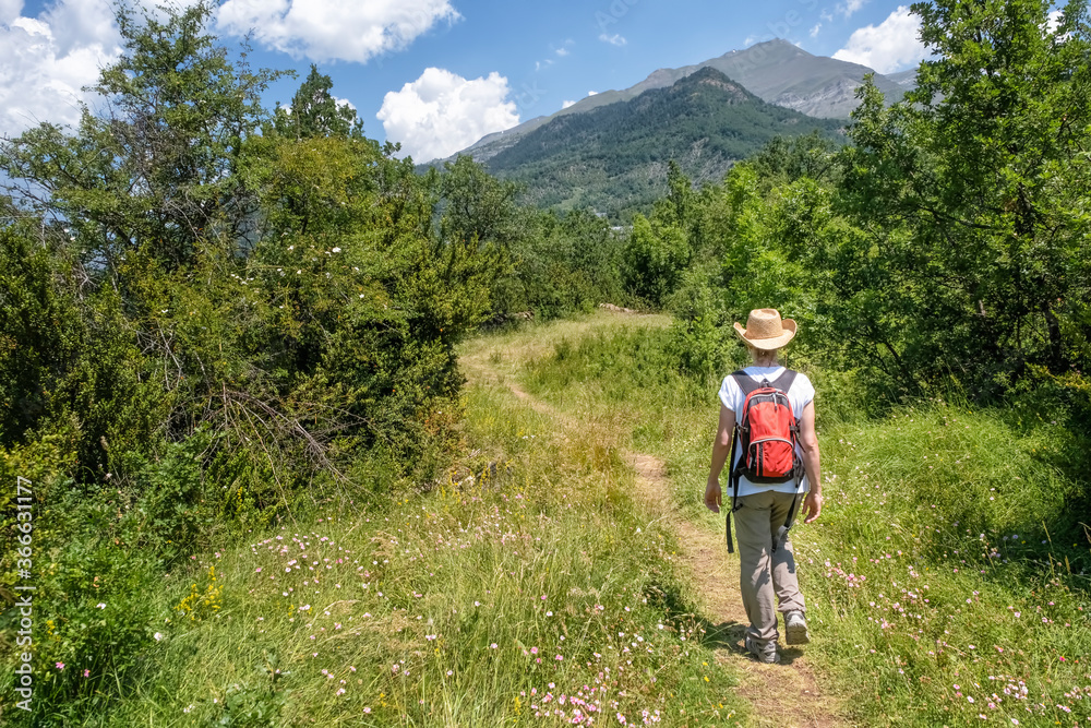 woman walking along a mountain path with a straw hat and a red backpack seen from behind