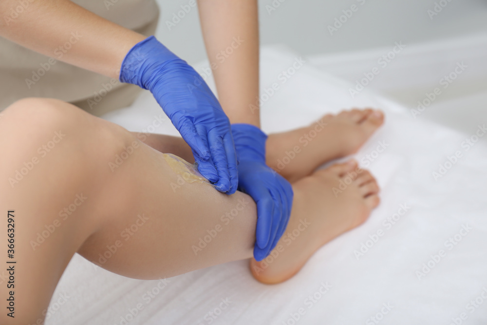 Woman getting wax epilation of legs in salon, closeup