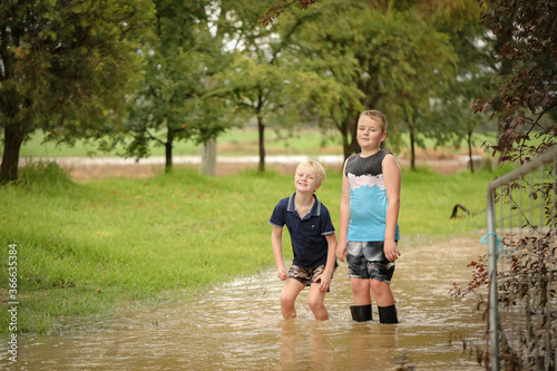 Two young brothers playing in flooded creek wearing gumboots in water