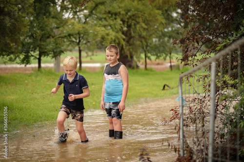 Two young brothers walking along flooded creek wearing gumboots in water