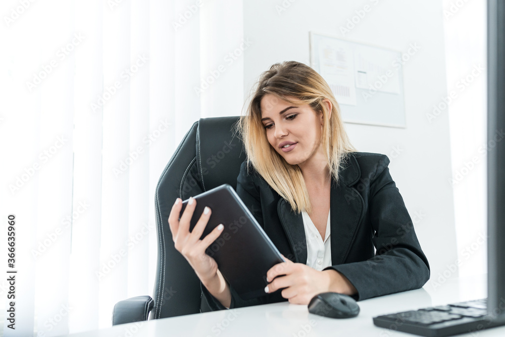 Successful blonde businesswoman sitting at work desk and holding tablet. Successful blonde businesswoman sitting at work desk and holding tablet.