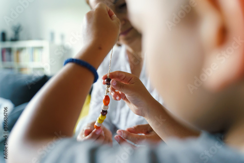 Fototapeta Back view of unknown caucasian child playing with string and wooden pearls by hi
