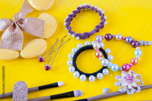 Hair bands, beads, cosmetic brushes and hair clips on a yellow background