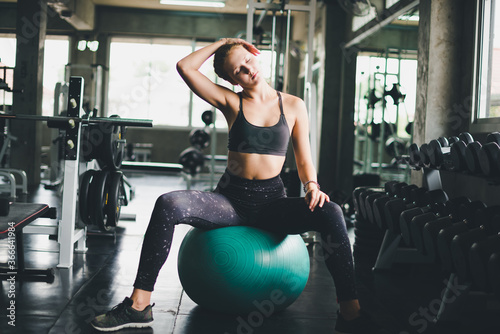 A beautiful woman wearing a sports shirt, stretching and relaxing with a rubber ball, yoga or exercise ball.