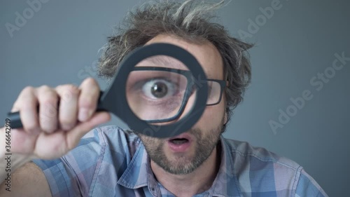 a curious funny surprised Middle-aged  man who is looking at the camera through a magnifying glass. Humorous portrait of a crazy man with no cut hair. photo