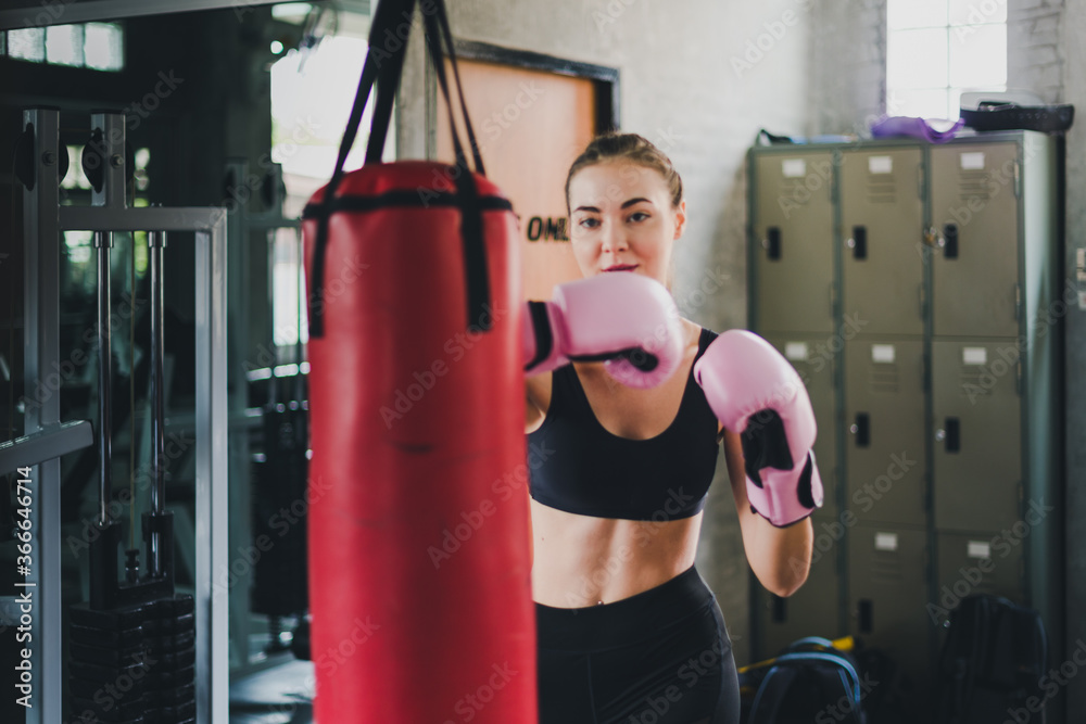 Beautiful fitness boxing gym. She wears a pink boxing glove and wears exercise. Sandbag is a pair of punches.