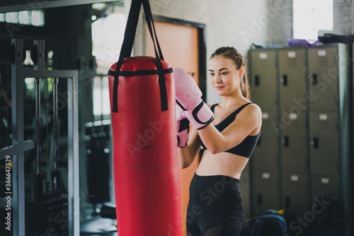 Beautiful fitness boxing gym. She wears a pink boxing glove and wears exercise. Sandbag is a pair of punches.