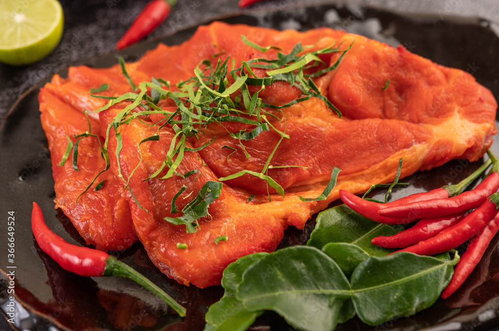 Marinated pork used in cooking, complete with chili peppers Kaffir lime leaves in a black plate Marinated pork used in cooking, complete with chili peppers Kaffir lime leaves in a black plate