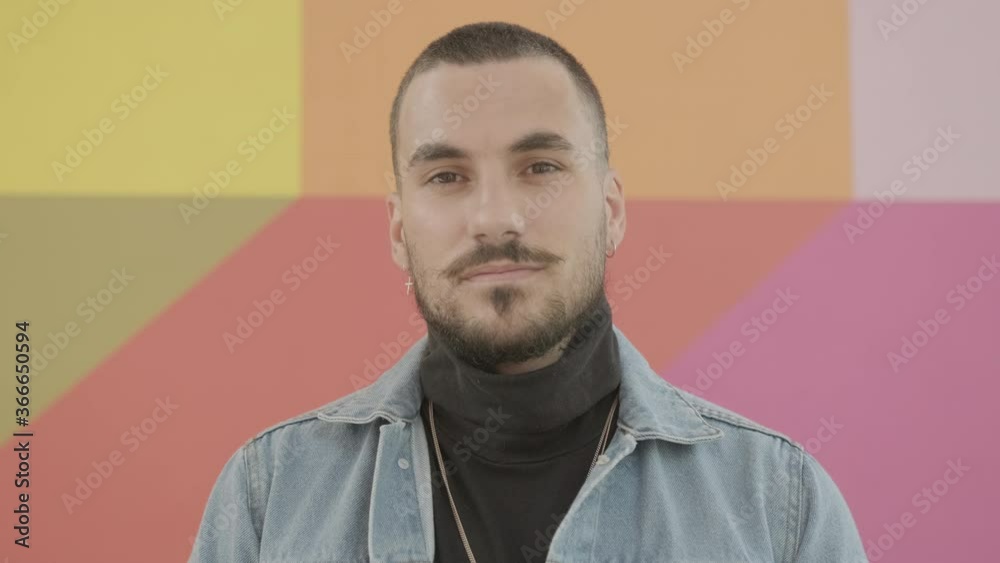 Portrait of young adult male with beard and moustache looking at camera confident against colourful wall