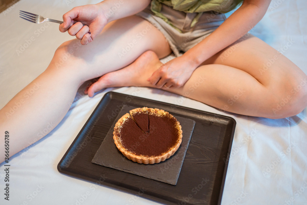 A top view of young pretty Asian woman eating delicious chocolate tart on bed