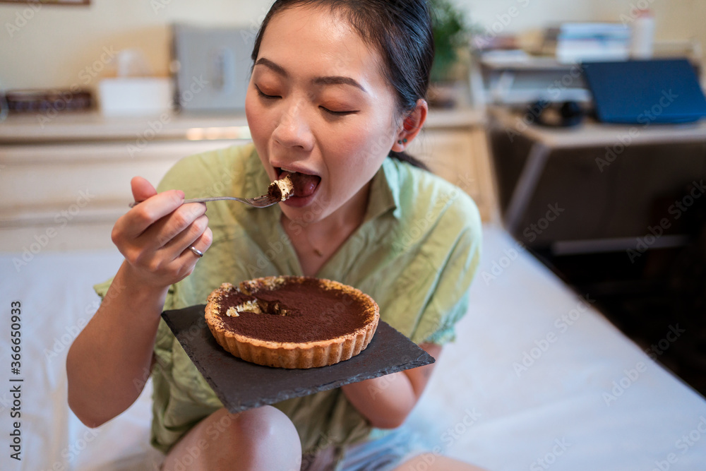 Young pretty Asian woman enjoying delicious chocolate tart on bed