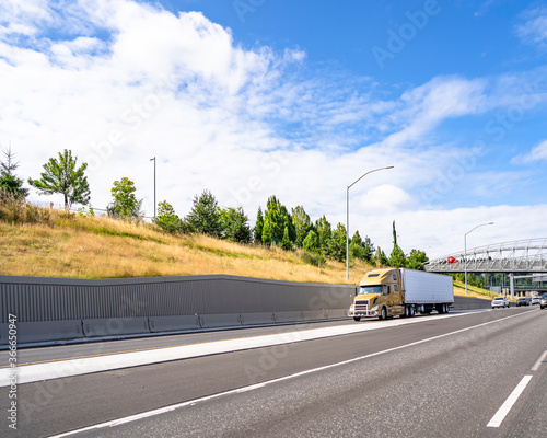 Big rig semi truck with refrigerator semi trailer transporting cargo driving on the wide highway with bridge and wall on the sidehill photo