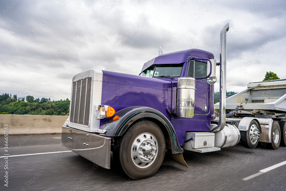 Bright purple classic big rig semi truck with chrome accessories transporting cargo in tip semi trailer for carry heavy freights