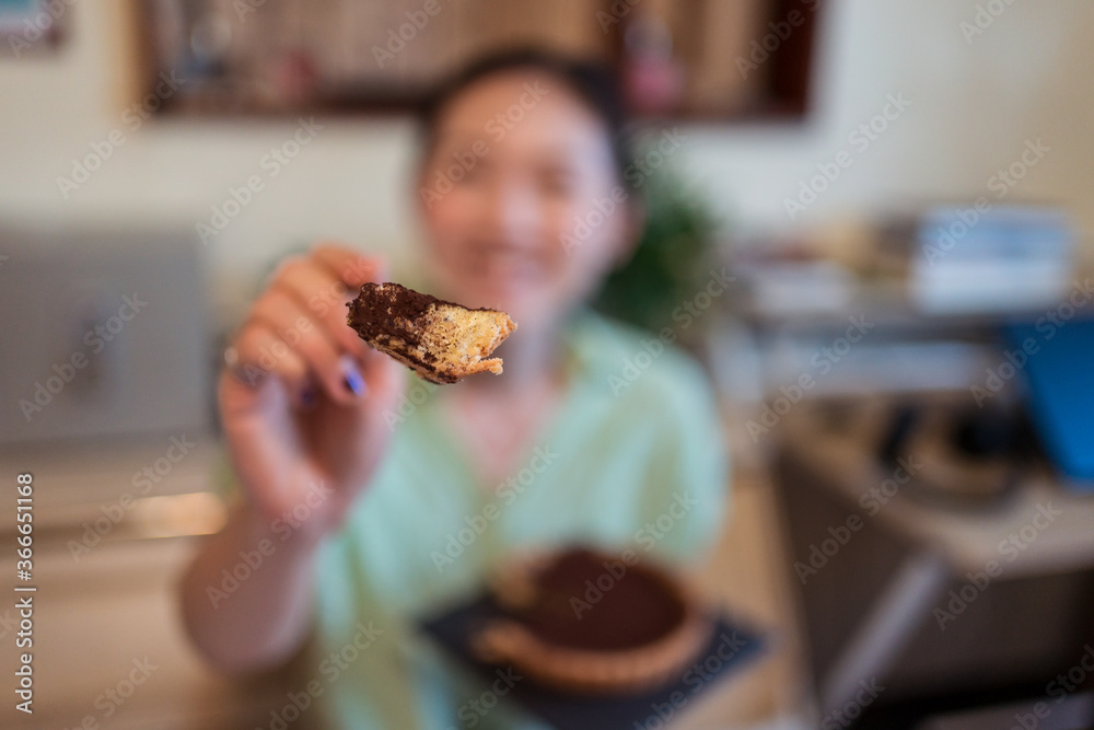 Young pretty Asian woman eating delicious chocolate tart lying on bed