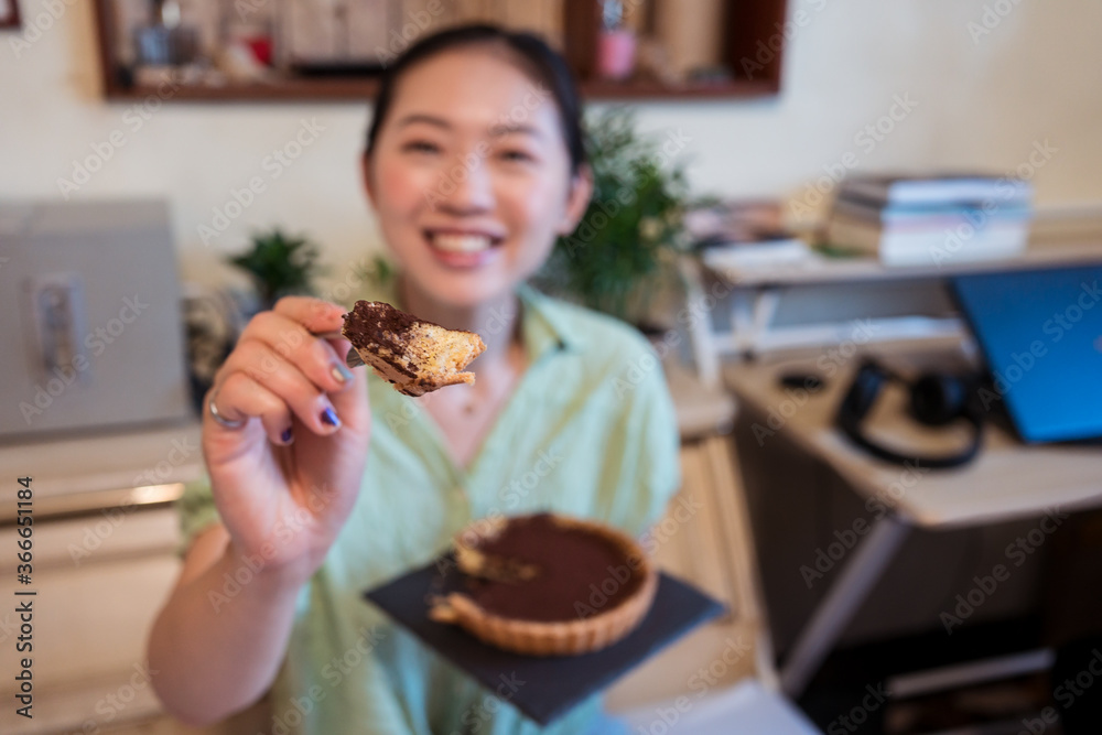 Young pretty Asian woman eating delicious chocolate tart lying on bed