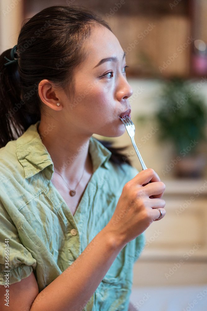 Young pretty Asian woman eating delicious chocolate tart on bed